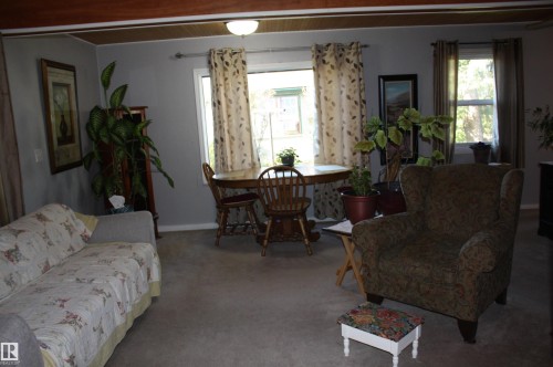 Interior living area featuring a wood-beam ceiling, ceiling-mounted light fixture, and windows with metal rod hardware - 5012 49 Ave, Radway, AB 