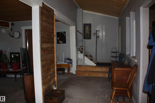 Interior space featuring exposed wood accent paneling, wood-plank ceiling, and multi-level floor plan with wood steps - 5012 49 Ave, Radway, AB 