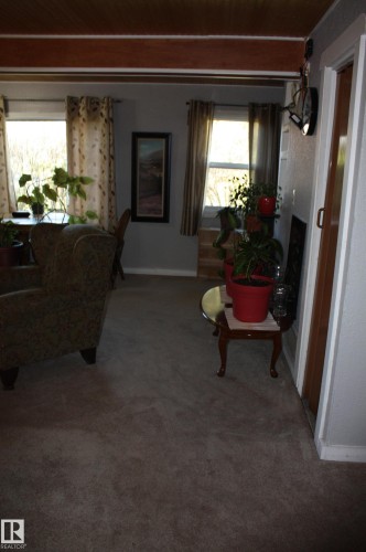 Living area featuring exposed wooden ceiling beams, neutral carpeting, and multiple windows - 5012 49 Ave, Radway, AB 
