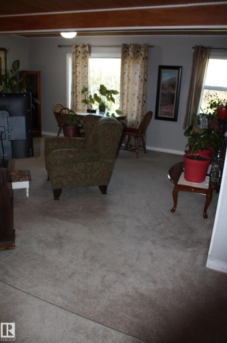Living area featuring exposed wood ceiling beams, wall-to-wall carpeting, and large windows - 5012 49 Ave, Radway, AB 