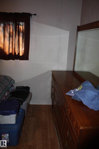 Interior space featuring wood-finish flooring and a single window with a mounted curtain rod - 5012 49 Ave, Radway, AB 