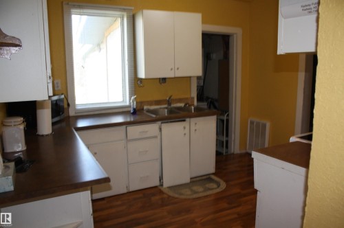 Kitchen featuring white cabinetry, wood-finish flooring, a double-basin stainless steel sink, and laminate countertops - 5012 49 Ave, Radway, AB 