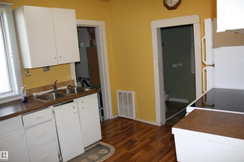 Kitchen featuring wood-finish flooring, dual-basin stainless steel sink, flat-panel white cabinetry, and dark solid-surface countertops - 5012 49 Ave, Radway, AB 
