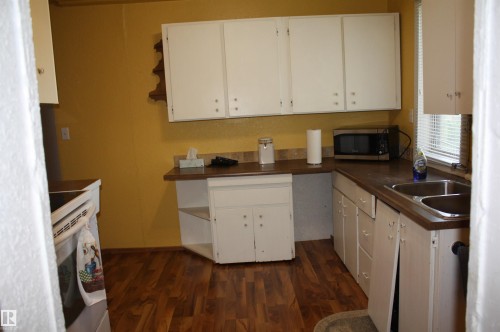 Kitchen featuring wood-finish flooring, white cabinetry, a dual-basin stainless steel sink, and laminate countertops - 5012 49 Ave, Radway, AB 
