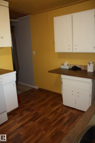 Kitchen area featuring white cabinetry, wood-finish flooring, and a dedicated surface with tile backsplash - 5012 49 Ave, Radway, AB 
