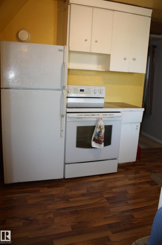 Kitchen area featuring white cabinetry, a freestanding refrigerator, an electric range, and wood-finish flooring - 5012 49 Ave, Radway, AB 