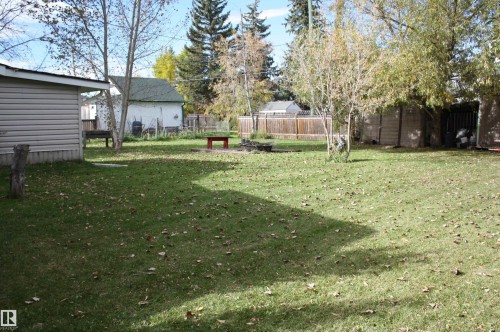 Expansive green lawn with scattered leaves, mature trees, and a wooden perimeter fence - 5012 49 Ave, Radway, AB 