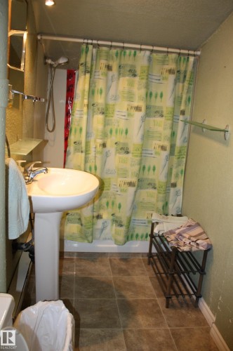 White pedestal sink with a chrome faucet, shower enclosure, and neutral-toned floor tile - 5012 49 Ave, Radway, AB 