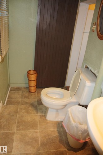 Bathroom featuring square floor tile, a white porcelain toilet, and a vertical wood-paneled door - 5012 49 Ave, Radway, AB 