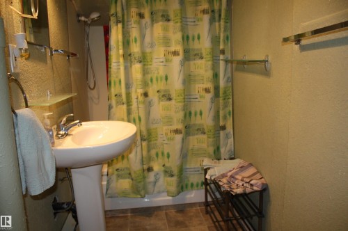 Bathroom featuring a white pedestal sink, chrome fixtures, a shower-tub combination, and tiled flooring - 5012 49 Ave, Radway, AB 