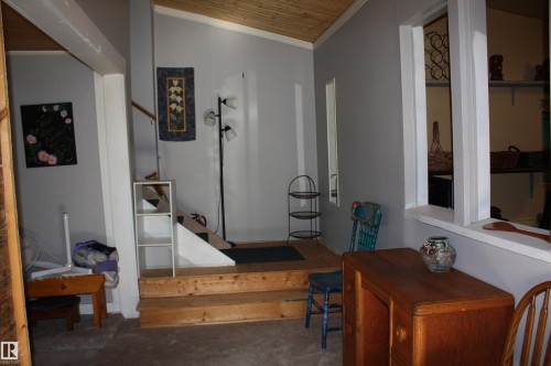 Interior area featuring a wood-plank ceiling, structural staircase with wooden steps, and a built-in pass-through wall opening - 5012 49 Ave, Radway, AB 