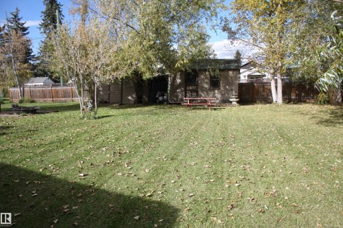 Expansive backyard featuring a manicured lawn, established trees, a storage shed, and perimeter fencing - 5012 49 Ave, Radway, AB 