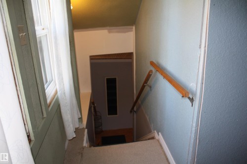 Staircase featuring carpeted treads, painted walls, and a wood handrail with metallic brackets - 5012 49 Ave, Radway, AB 