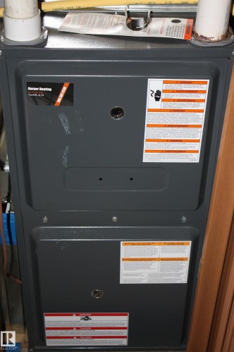 High-efficiency furnace unit featuring a matte gray metal exterior, dual PVC exhaust venting, and factory-applied safety and identification labeling - 5012 49 Ave, Radway, AB 