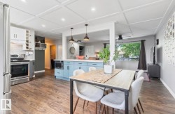 Wood-finish flooring throughout, coffered ceiling with recessed lighting, and a kitchen featuring stainless steel appliances, subway tile backsplash, and light blue lower cabinetry - 