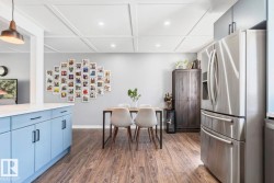 Wood-finish flooring throughout, coffered ceiling with recessed lighting, stainless steel refrigerator, light blue cabinetry with dark hardware, and light gray upper cabinetry - 