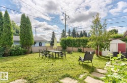 Expansive rear yard featuring a manicured lawn, established landscaping, privacy fencing, a storage shed, and stone paver pathways - 