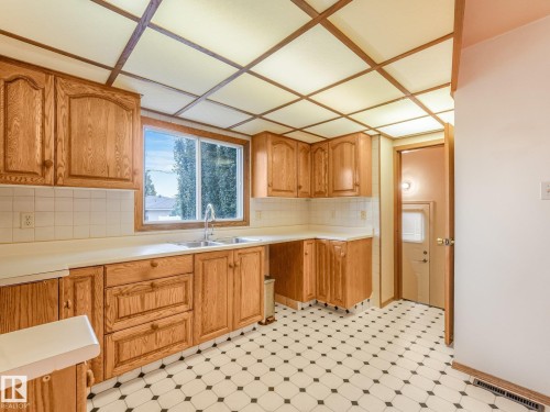 Wood cabinetry, white tile backsplash, light-toned countertops, double basin stainless steel sink with a gooseneck faucet, and patterned floor tile - 5904 94 Avenue Nw, Edmonton, AB 
