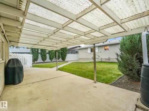 Concrete patio with a translucent covered pergola, leading to a manicured lawn and privacy plantings - 5904 94 Avenue Nw, Edmonton, AB 