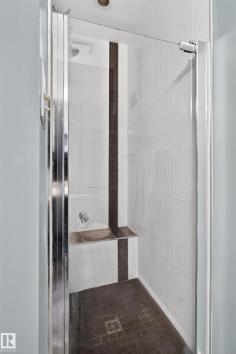 Glass-enclosed shower with white tiled walls, a dark tiled accent stripe, a built-in bench, and dark tiled flooring - 1519 104 Street Nw, Edmonton, AB 