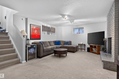 Carpeted flooring, painted white brick fireplace, staircase with carpeted treads, white painted walls, and an egress window - 1519 104 Street Nw, Edmonton, AB 