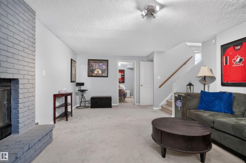 Painted brick fireplace, light-toned carpeting, white interior doors, and a wood handrail on the staircase - 1519 104 Street Nw, Edmonton, AB 
