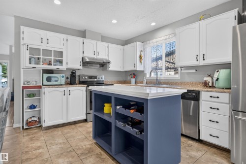 White cabinetry with dark hardware, a center island featuring built-in wine storage, stainless steel appliances, a tile floor, and a double basin sink - 1519 104 Street Nw, Edmonton, AB 