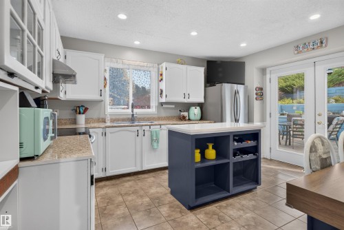 Kitchen featuring white cabinetry, a central island with integrated storage, tile flooring, and light-toned countertops - 1519 104 Street Nw, Edmonton, AB 