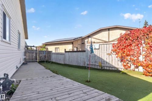 Backyard featuring a synthetic turf putting green, a wooden deck, concrete patio, and a wooden fence with mature foliage - 1519 104 Street Nw, Edmonton, AB 