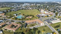 Expansive suburban landscape with varied residential structures, abundant green spaces, a commercial building complex, and multiple roadways - 