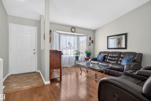 Open concept living area featuring hardwood-finish flooring, a bay window with natural light, and a white paneled entry door - 1519 104 Street Nw, Edmonton, AB 