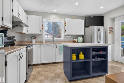 Kitchen featuring white cabinetry with dark hardware, a center island with integrated shelving, stainless steel appliances, and tile flooring - 1519 104 Street Nw, Edmonton, AB 