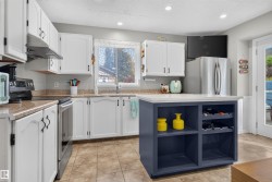 Kitchen featuring white cabinetry with dark hardware, a center island with integrated shelving, stainless steel appliances, and tile flooring - 