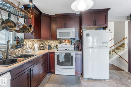 Kitchen featuring dark wood-finish cabinetry, mosaic tile backsplash, solid surface countertops, and an integrated double basin sink - 4103 44 Avenue, Stony Plain, AB 