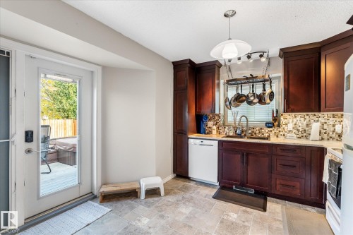 Rich wood-finish cabinetry, tile flooring, mosaic tile backsplash, and a contemporary pendant light fixture - 4103 44 Avenue, Stony Plain, AB 
