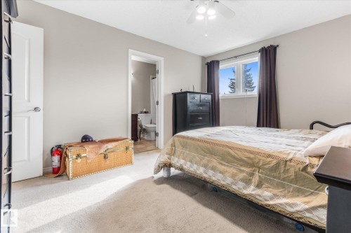 Carpeted room with a ceiling fan, a window with dark curtains, and an open doorway leading to a bathroom - 4103 44 Avenue, Stony Plain, AB 