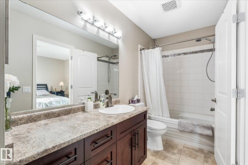 Bathroom featuring a dark wood-finish vanity with a stone-finish countertop, single basin sink, and a tiled tub/shower combination with decorative accent tiles - 4103 44 Avenue, Stony Plain, AB 