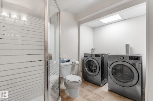 Glass-enclosed shower with frosted detailing, toilet, and a dedicated laundry area with appliances - 4103 44 Avenue, Stony Plain, AB 