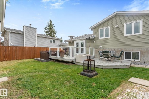 Expansive green yard featuring a wooden privacy fence, multi-level composite deck with glass railings, and dual exterior doors - 4103 44 Avenue, Stony Plain, AB 