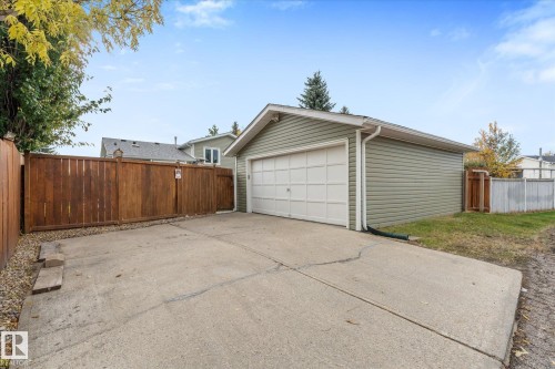 Detached garage with horizontal siding, white overhead door, concrete driveway, and wood privacy fencing - 4103 44 Avenue, Stony Plain, AB 