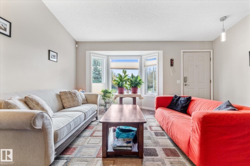 Living area featuring a bay window, wood-finish flooring, a paneled entry door, and a pendant light fixture - 4103 44 Avenue, Stony Plain, AB 
