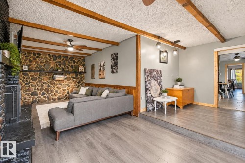 Stone accent wall with built-in shelving, wood-finish flooring, exposed ceiling beams, and a black slate fireplace surround - 62202 Rr 444, Rural Bonnyville M.D., AB 
