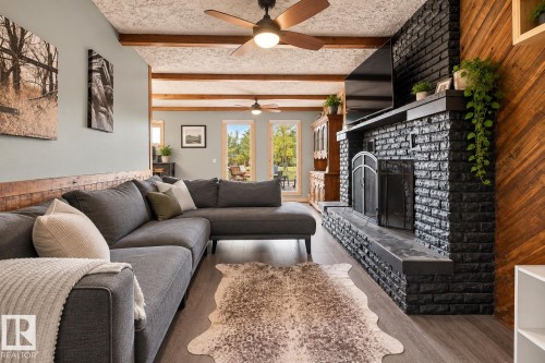 Living area featuring a floor-to-ceiling brick fireplace with a hearth, wood-finish flooring, exposed wood ceiling beams, and a decorative wood accent wall - 62202 Rr 444, Rural Bonnyville M.D., AB 