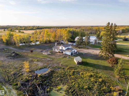 White exterior home with multiple outbuildings, bordered by mature trees and a natural water feature - 62202 Rr 444, Rural Bonnyville M.D., AB 