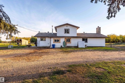 White exterior siding with a stone chimney, multiple windows, and a paved patio area - 62202 Rr 444, Rural Bonnyville M.D., AB 