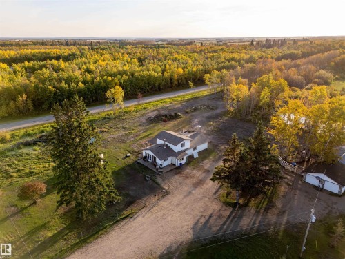 White exterior residence with dark roof, surrounded by mature trees, and an expansive gravel driveway - 62202 Rr 444, Rural Bonnyville M.D., AB 