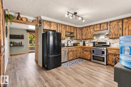 Kitchen featuring wood-finish cabinetry, wood-finish countertops, stainless steel appliances, a tile backsplash, and wood-finish flooring - 62202 Rr 444, Rural Bonnyville M.D., AB 