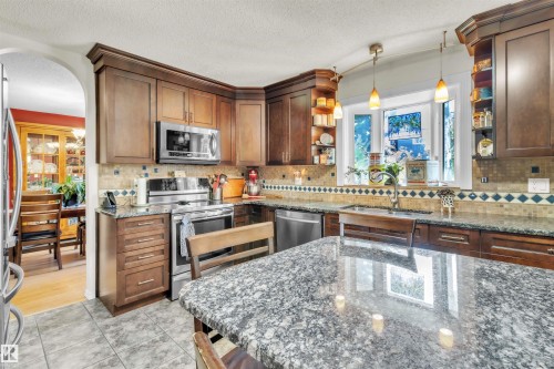 Kitchen featuring wood cabinetry, stainless steel appliances, speckled countertops, tile flooring, and a decorative tile backsplash - 76 Gariepy Crescent Nw, Edmonton, AB 