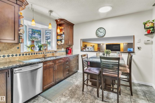 Kitchen featuring wood cabinetry, granite countertops, a tile backsplash, stainless steel dishwasher, and a bay window - 76 Gariepy Crescent Nw, Edmonton, AB 