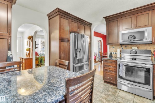 Kitchen featuring wood cabinetry, granite countertops, stainless steel appliances, and a tile backsplash - 76 Gariepy Crescent Nw, Edmonton, AB 